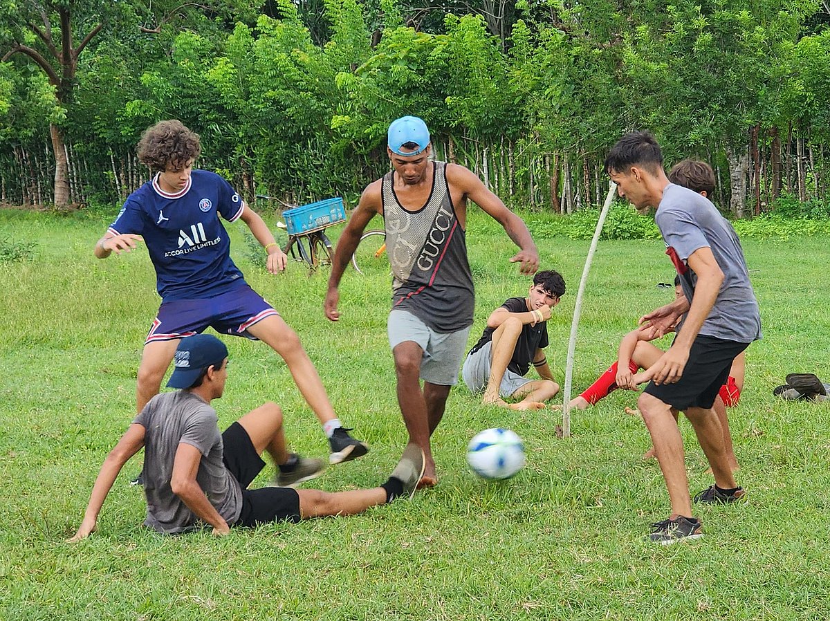 Eine Gruppe kubanischer Jugendlicher spielt auf einem grünen Rasen Fußball.