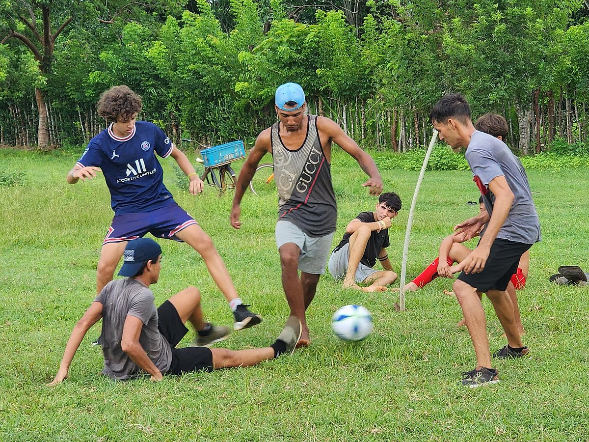 A group of Cuban youths are playing football on a green lawn.