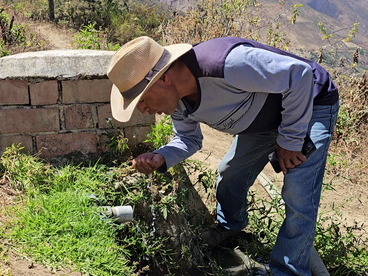 Ein peruanischer Mann beugt sich über eine Wasserleitung und führt frisches Wasser mit der Hand zum Mund.